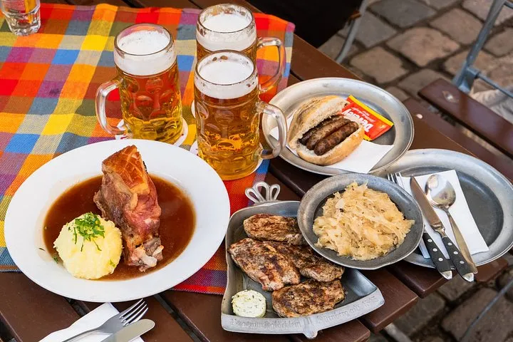 A plate of roast pork shoulder with dumpling, small sausages and two glasses of beer on a checked tablecloth