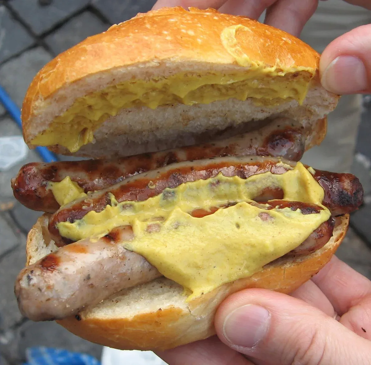 Three small grilled Nuremberg sausages with mustard in a bread roll held in one hand