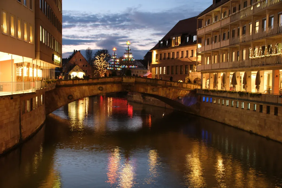 The stone arch of the Fleischbrücke over the Pegnitz at dusk with Christmas lights on the buildings