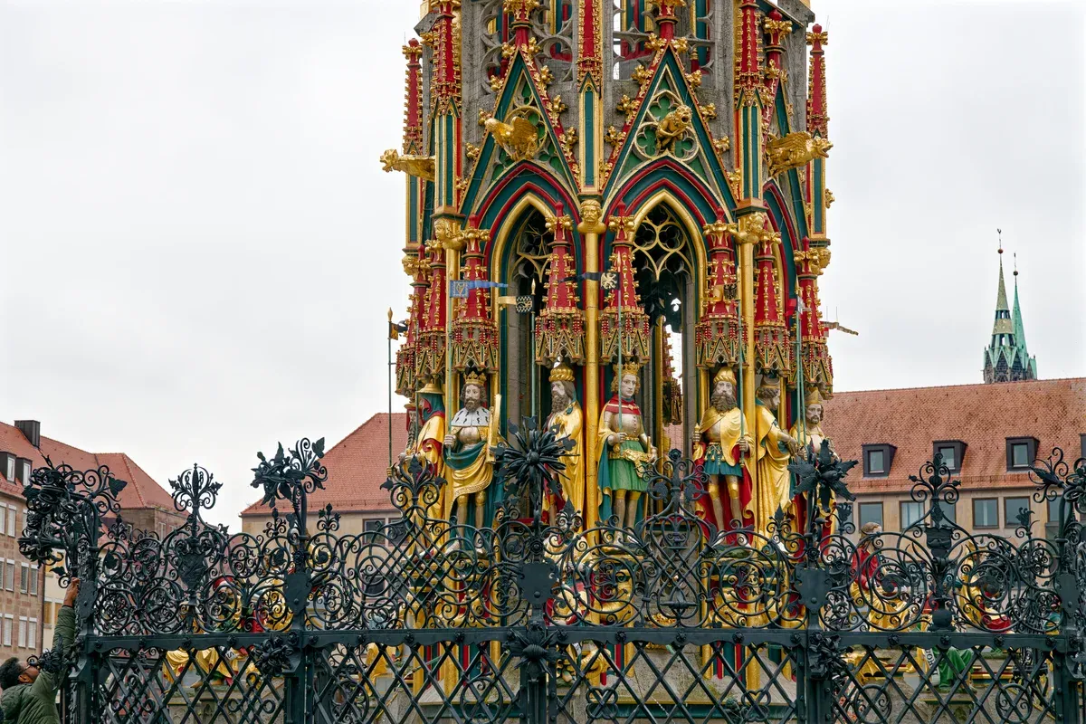 The painted gothic spire of the Schöner Brunnen behind its wrought-iron fence on the Hauptmarkt